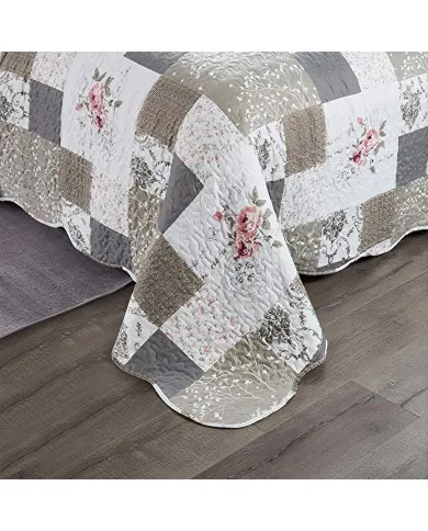 A patchwork quilt in beige and khaki featuring floral patterns, vermicelli stitching and scalloped edging.