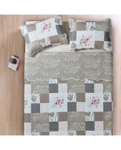 Quilted bedspread with a floral patchwork design in beige, complemented by matching decorative pillows.