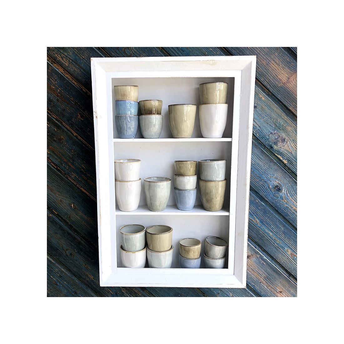 A white-framed shelf displays various boho coffee cups in shades of grey, beige, and white.