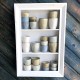 A white-framed shelf displays various boho coffee cups in shades of grey, beige, and white.
