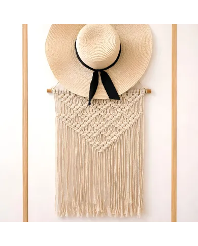 Een breedgerande strooien hoed met een zwart lint hangt over een macramé vintage wandhanger met gedetailleerde knoopontwerpen.