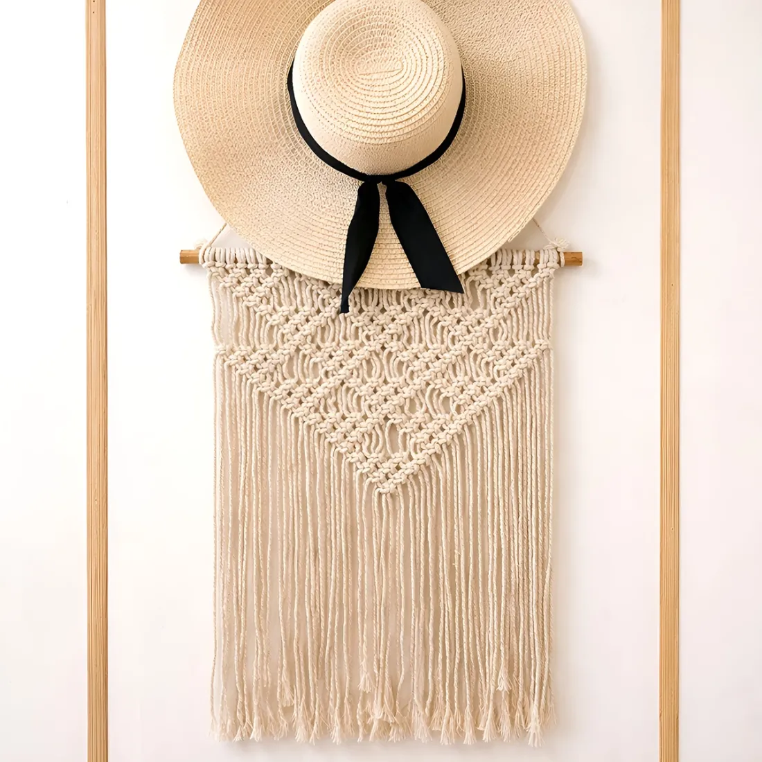 A wide-brimmed straw hat with a black ribbon hangs over a macramé wall hanging featuring intricate knot designs.