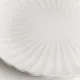 Close up of a white dinner plate with a subtle fluted texture and scalloped edge.