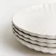 Set van vier witte dinerborden met een subtiel geribbeld patroon en een geschulpte rand.
