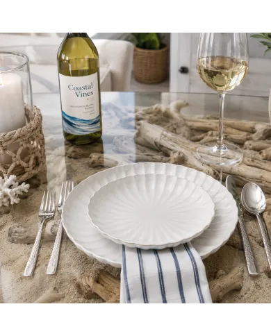 Witte dinerborden gedekt met bestek, een fles en een glas witte wijn.