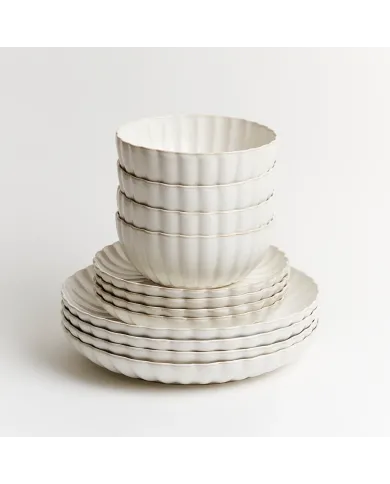 Stack of white dinner plates and soup bowls with scalloped edges.