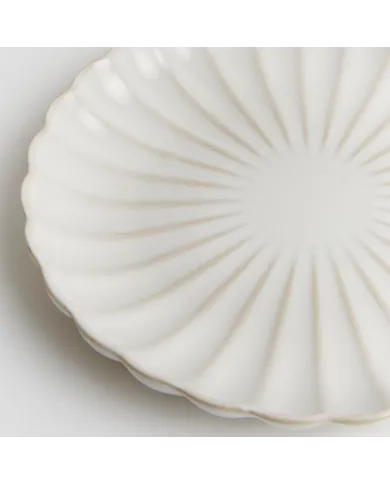 Close up of a white side plate with a subtle fluted texture and scalloped edge.