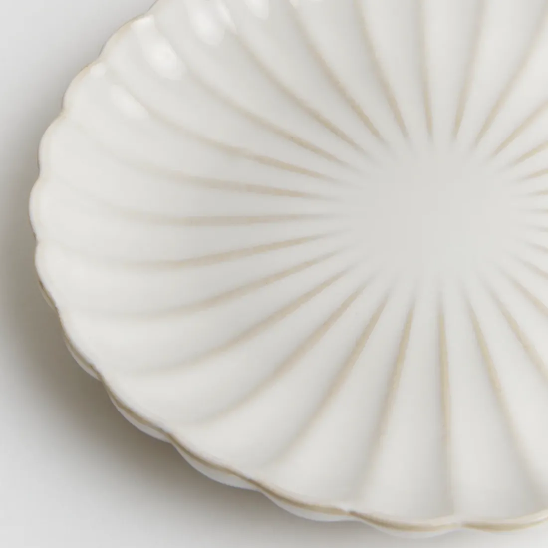 Close-up van een van de witte gebaksbordjes met een subtiel geribbeld patroon en een geschulpte rand.