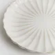 Close up of a white side plate with a subtle fluted texture and scalloped edge.