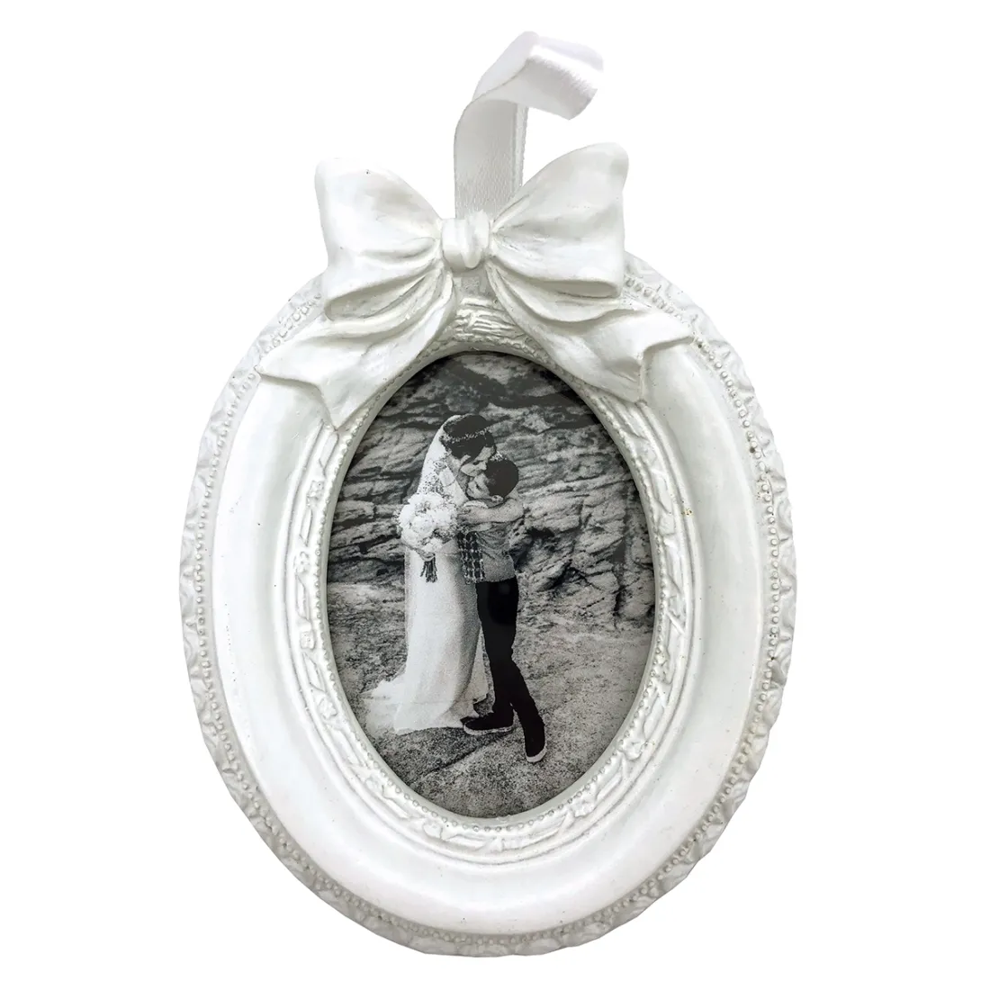 Witte, ovale vintage fotolijst met een strik, met daarin een zwart-witfoto van een bruid en een kind die elkaar omhelzen.