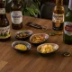 Borrelschaaltjes met olijven, noten, mosterd en kaas, vergezeld van flesjes bier.