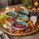 A platter featuring dipping bowls with cheeses, bread, grapes, and various appetizers.