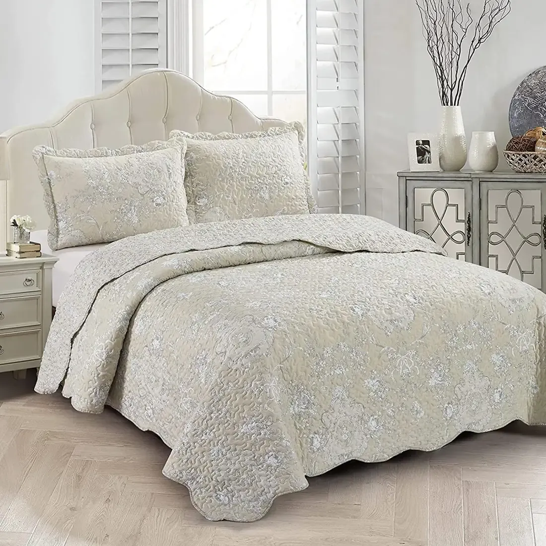 Elegant beige quilt with subtle floral print, scalloped edges and matching pillowcases on a cozy bed.