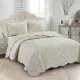 Elegant beige quilt with subtle floral print, scalloped edges and matching pillowcases on a cozy bed.