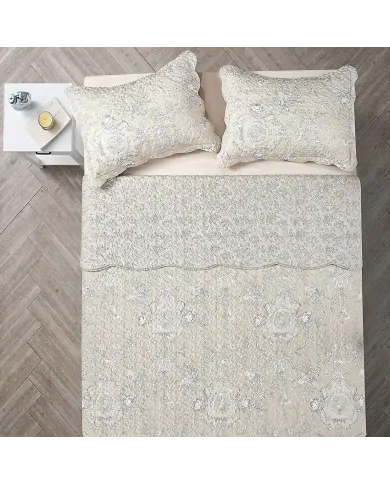 Top view of a beige quilt on a bed, complemented by matching decorative pillows.
