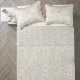 Top view of a beige quilt on a bed, complemented by matching decorative pillows.