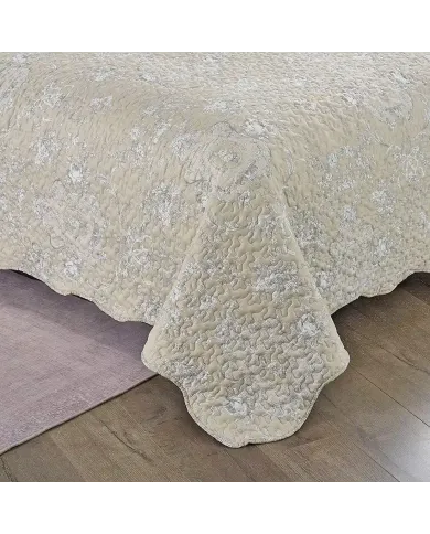 Detail of a beige quilt showcasing a subtle floral toile pattern, vermicelli stitching and scalloped edging.