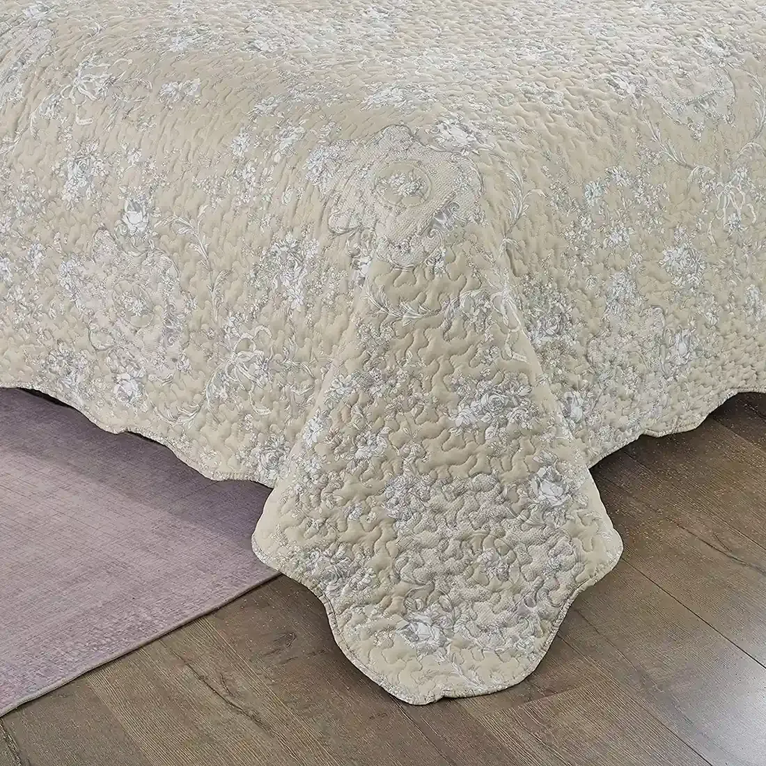 Detail van een beige bedsprei met een subtiel toile-bloempatroon, vermicellistiksels en schulprand.