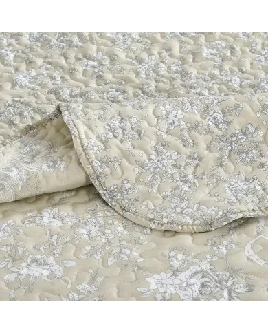 Close-up van een beige bedsprei met een toile-bloempatroon en fijne stiksels.