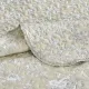 Close-up van een beige bedsprei met een toile-bloempatroon en fijne stiksels.