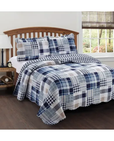 Een patchwork blauwe bedsprei met wit en beige tinten op een bed met bijpassende kussens.