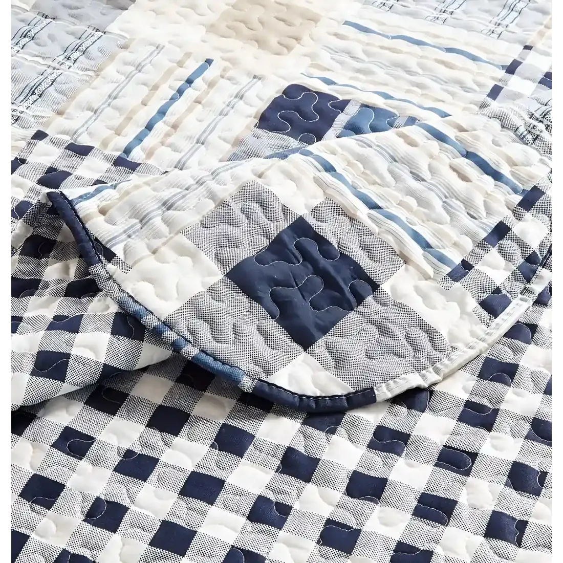 Close-up van een blauwe bedsprei, in blauw en wit patchwork met een verfijnde stikselstructuur.