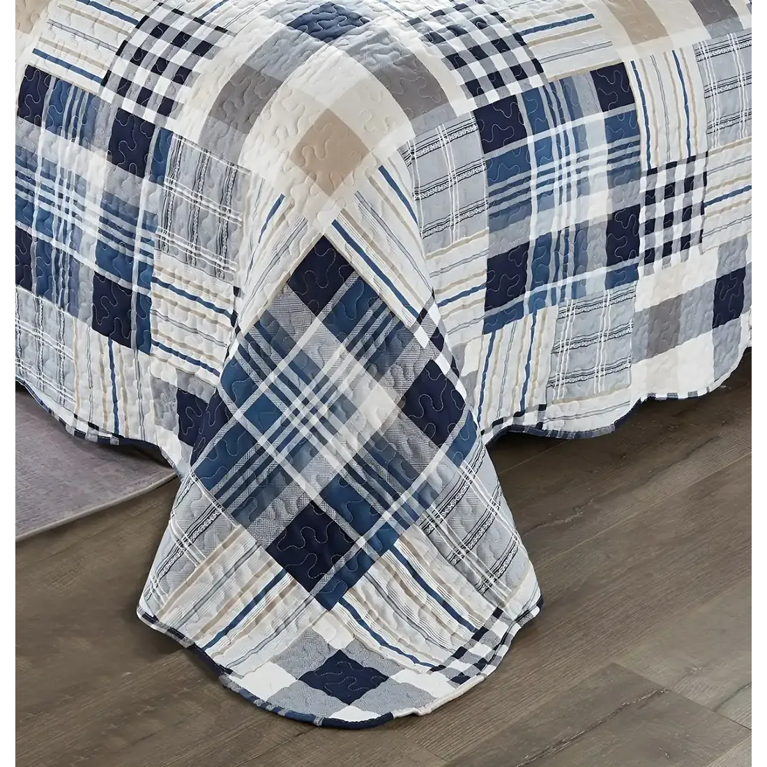 Detail van een blauwe bedsprei met blauw en wit patchwork, vermicellistiksels en geschulpte randen.