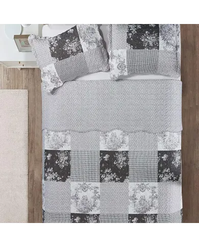 Top view of a patchwork grey quilt on a bed, complemented by matching decorative pillows.