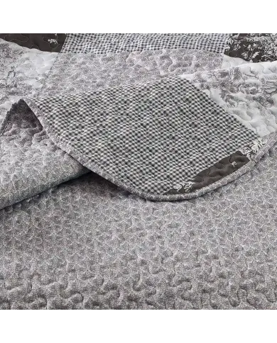 Close-up van een grijze bedsprei met een klein grijs toile-bloempatroon en fijne stikstructuur.