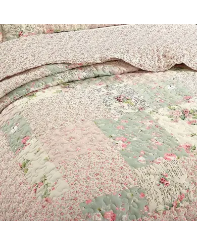 Close-up of a floral quilt, showcasing pink and sage patchwork with a delicate stitching texture.