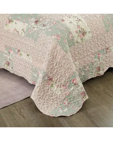 Detail of a floral quilt showcasing pink and sage patchwork, vermicelli stitching and scalloped edging.