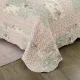 Detail of a floral quilt showcasing pink and sage patchwork, vermicelli stitching and scalloped edging.