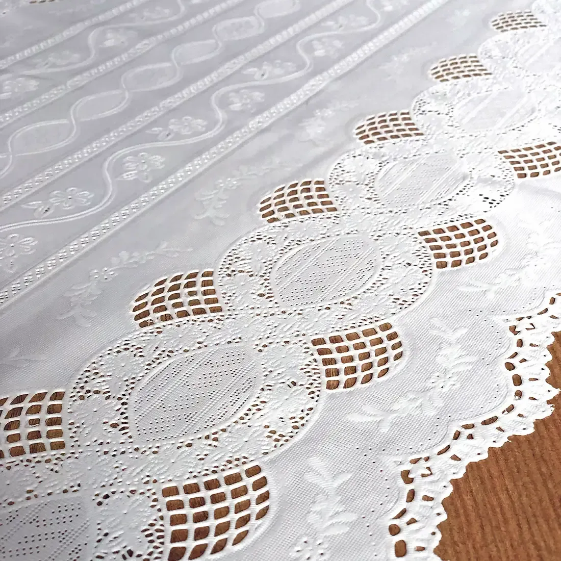 Close up detail of a white table runner made from vinyl with lace details and scalloped edges.