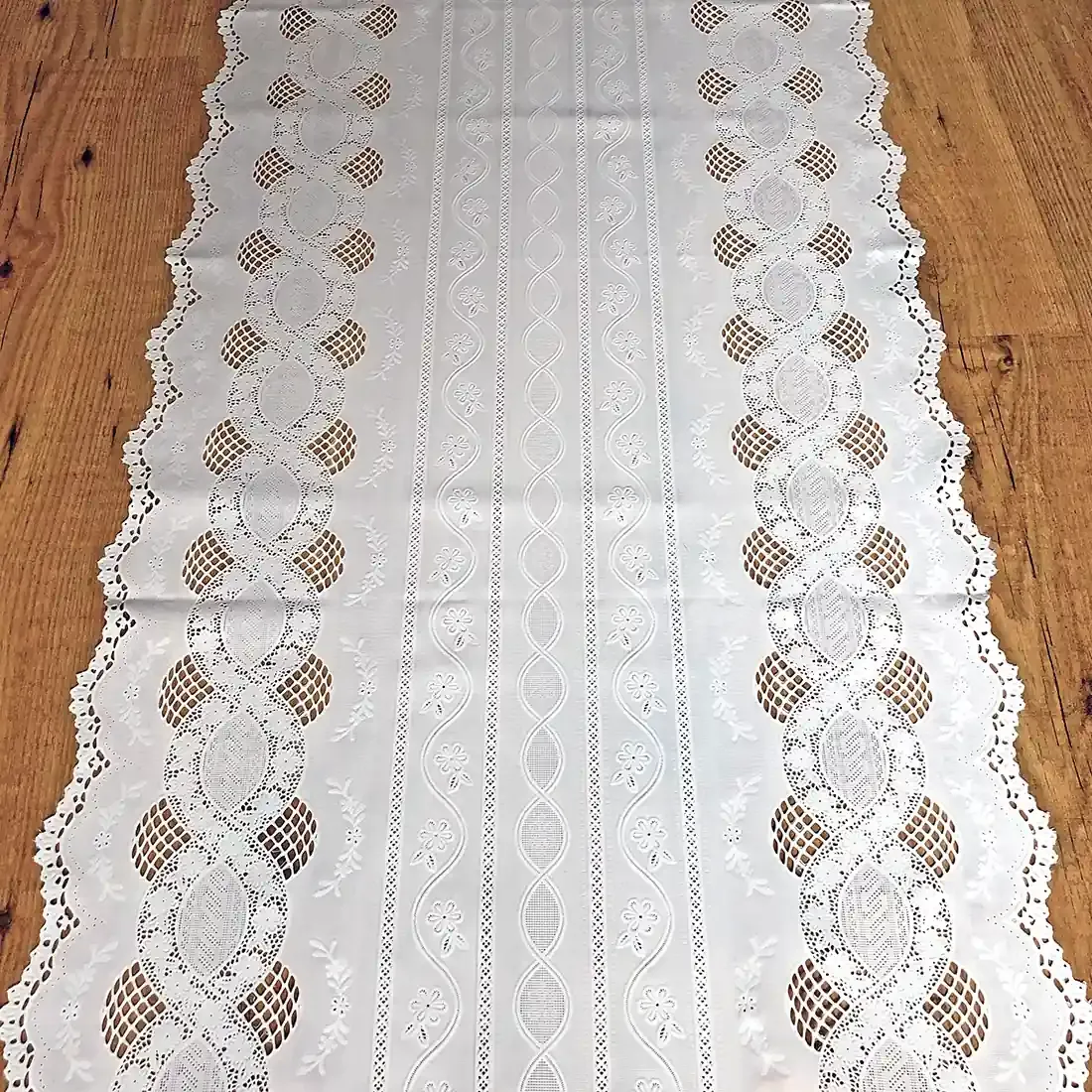 Close up detail of a white table runner made from vinyl with lace details and scalloped edges.