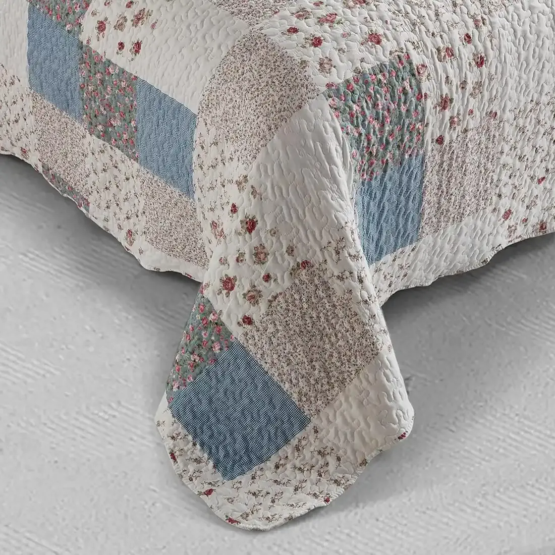 Detail of a floral bedspread showcasing blue and white patchwork, vermicelli stitching and scalloped edging.