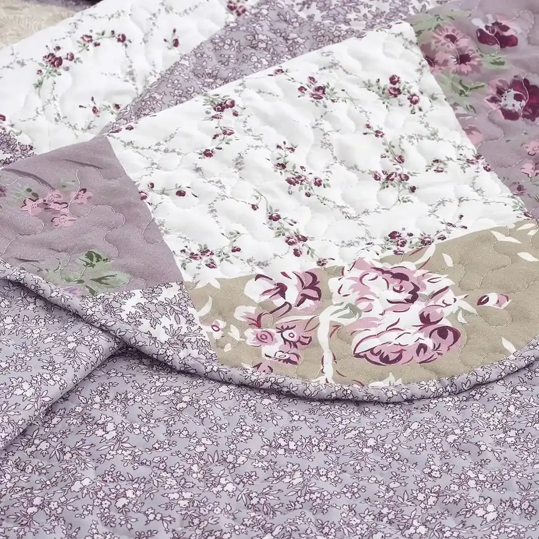 Close-up of a floral quilt, showcasing a patchwork lavender print with a delicate stitching texture.
