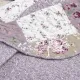 Close-up of a floral quilt, showcasing a patchwork lavender print with a delicate stitching texture.