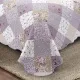 Detail of a floral quilt showcasing a patchwork lavender print, vermicelli stitching and scalloped edging.