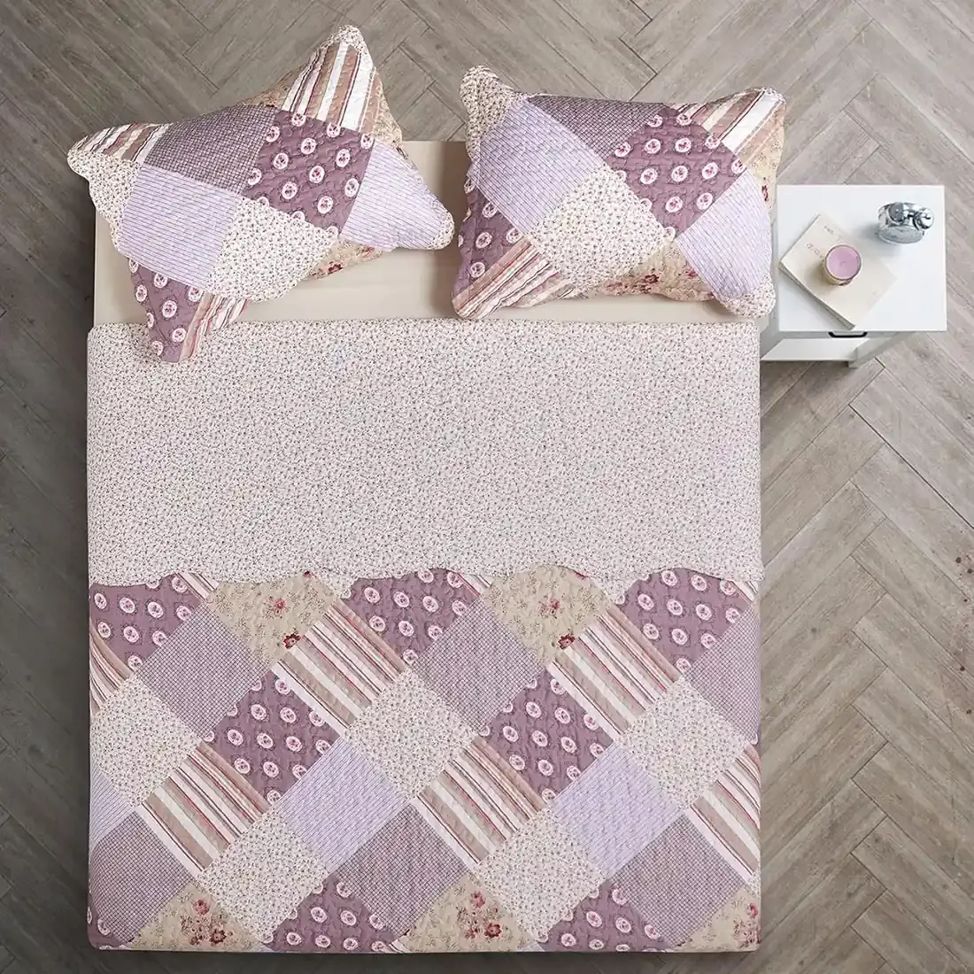 Bovenaanzicht van een bedsprei oud roze in patchwork op een bed, aangevuld met bijpassende sierkussens.
