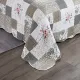 Een patchwork bedsprei beige en wit gekleurd, met bloemmotieven, vermicellistiksels en geschulpte randen.