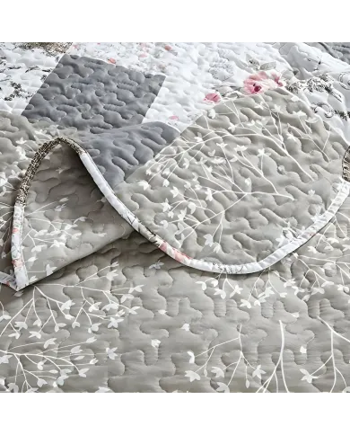 Close-up van een bedsprei beige en wit gekleurd, met bloemen en patronen en fijne stikselstructuur.