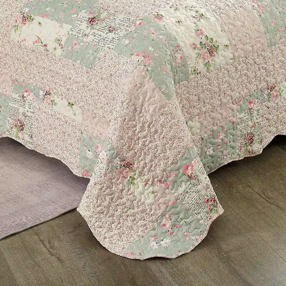 Detail of a floral quilt showcasing pink and sage patchwork, vermicelli stitching and scalloped edging.