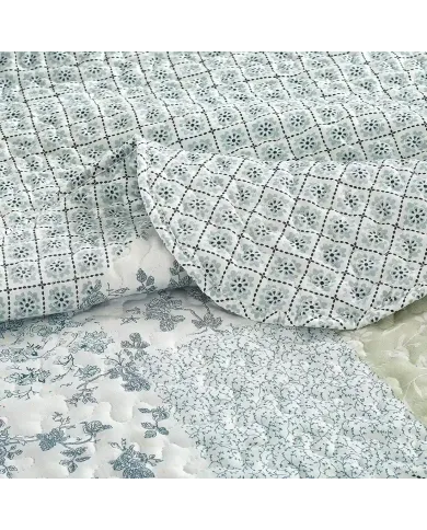 Close-up of a blue bedspread, showcasing blue and green tones with a delicate stitching texture.