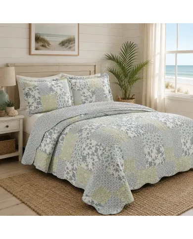 A quilt in blue and green tones on the bed in a well-lit bedroom with a sea view.
