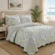 A quilt in blue and green tones on the bed in a well-lit bedroom with a sea view.