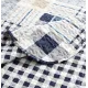 Close-up van een blauwe bedsprei, in blauw en wit patchwork met een verfijnde stikselstructuur.