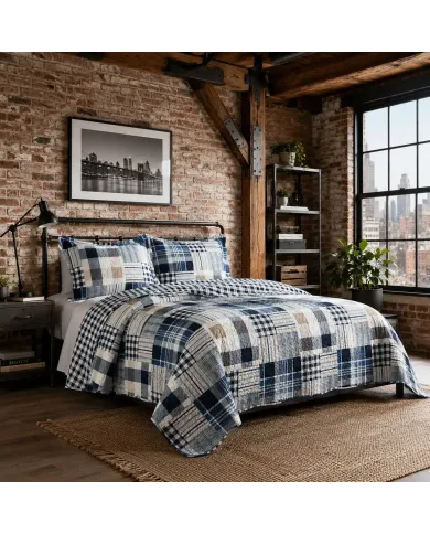 A blue patchwork quilt with white and beige tones on a bed with matching pillows.