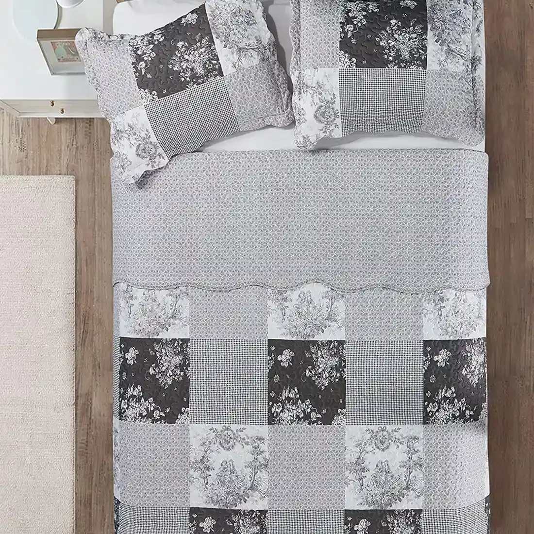 Top view of a patchwork grey quilt on a bed, complemented by matching decorative pillows.