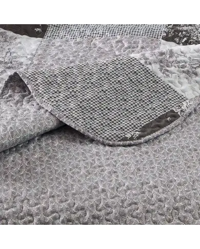 Close-up of a grey quilt, showcasing a small grey floral toile pattern with a delicate stitching texture.