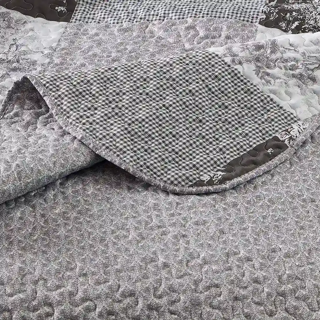 Close-up van een grijze bedsprei met een klein grijs toile-bloempatroon en fijne stikstructuur.
